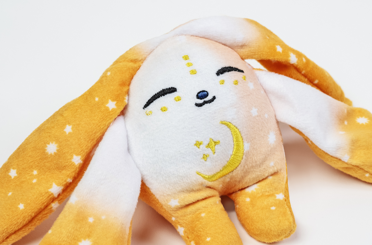 Ori Mini Wrist Hugger – Magnetic Sensory Plush with long orange and white star-patterned ears, a smiling face with closed eyes, and an embroidered crescent moon and stars on its belly.