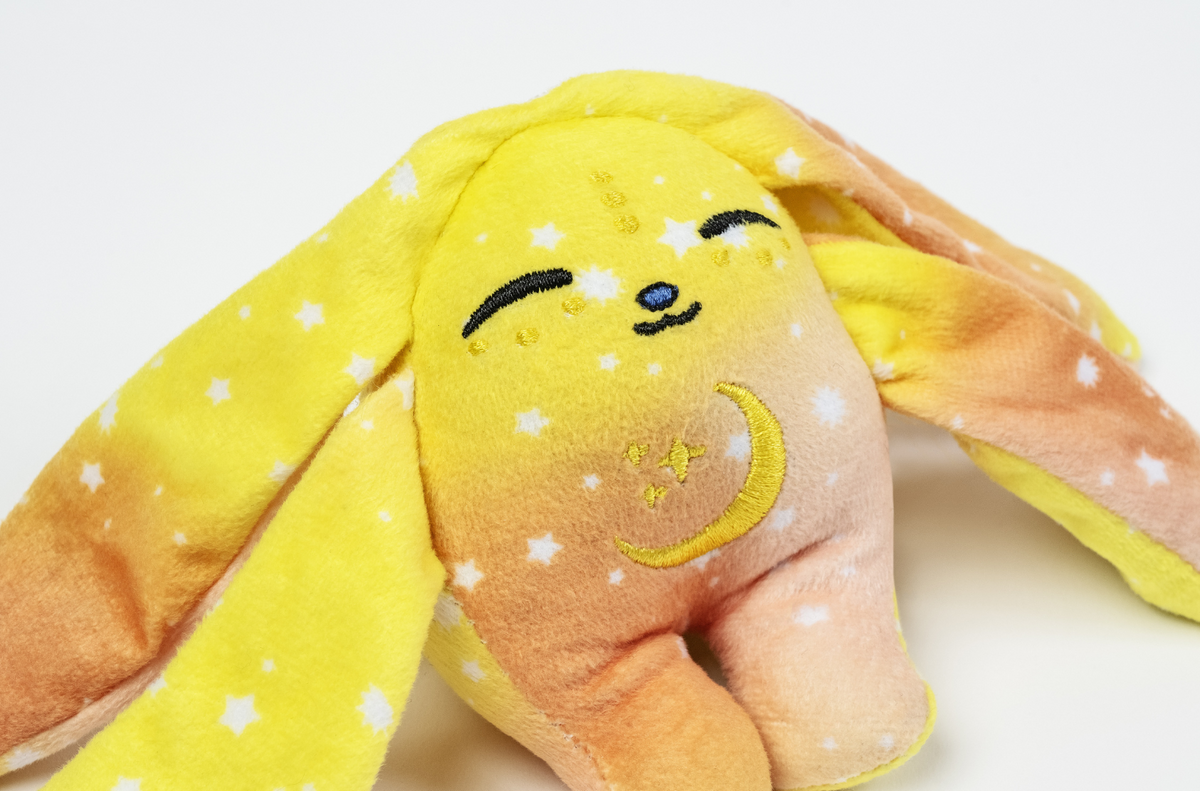 Spark Mini Wrist Hugger – Magnetic Sensory Plush, a pocket-sized rabbit with a yellow and orange ombré pattern, white stars, and an embroidered moon on its chest.