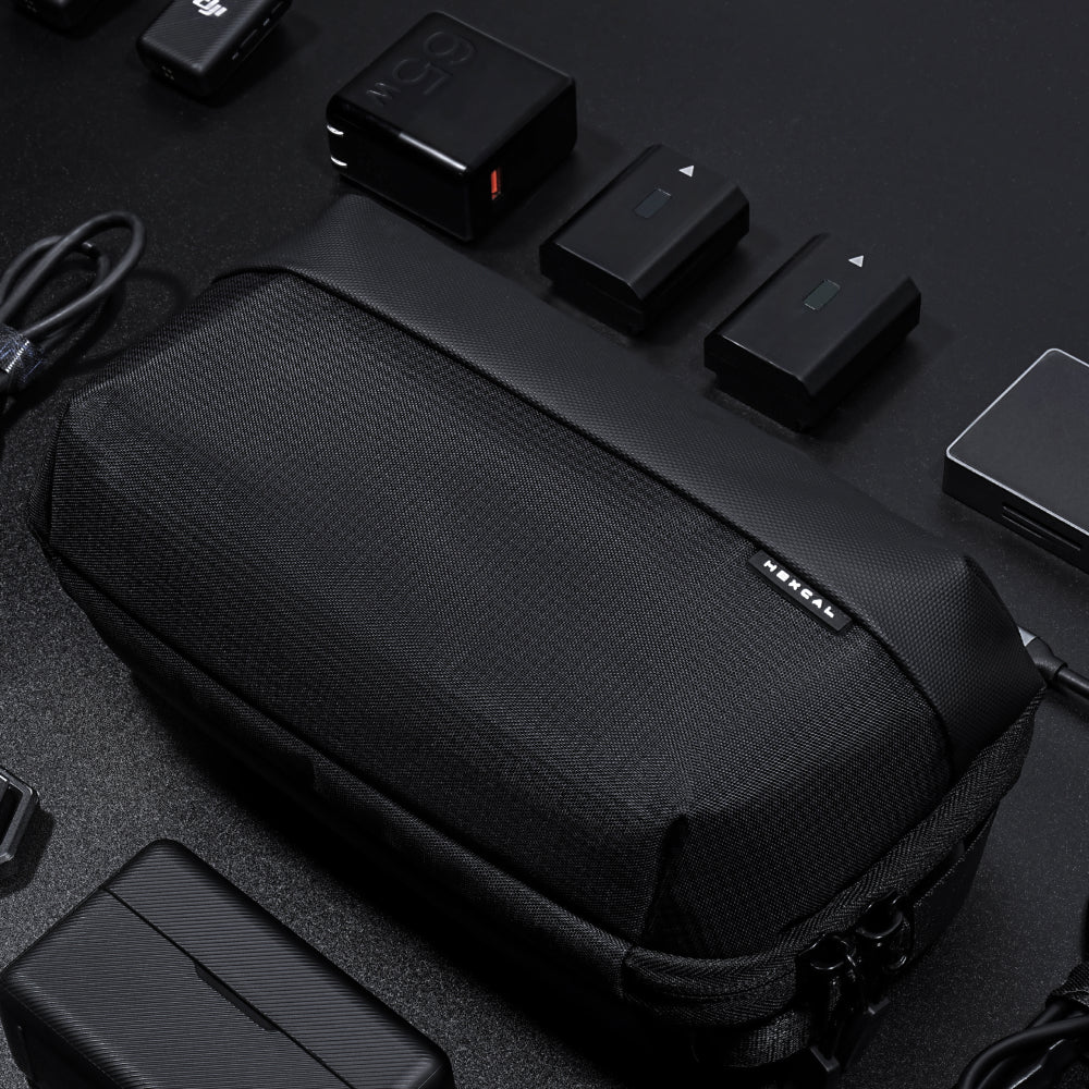 A Tech Pouch sits on a dark surface, neatly surrounded by camera batteries, chargers, cables, and electronic accessories.