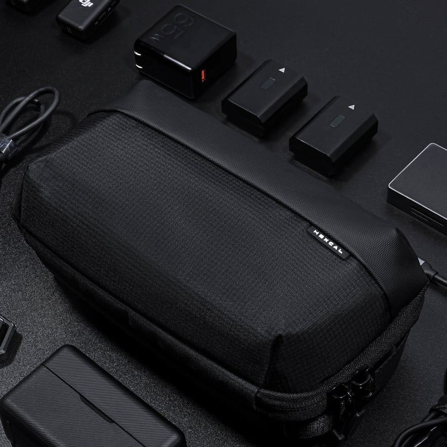 A Tech Pouch sits on a dark surface, neatly surrounded by camera batteries, chargers, cables, and electronic accessories.