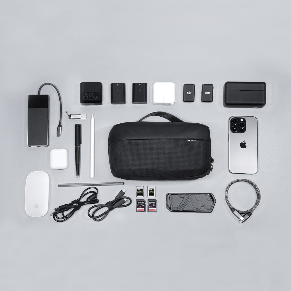 A neatly arranged flat lay features a Tech Pouch along with a smartphone, charging cables, adapters, memory cards, Apple Magic Mouse, digital pen, stylus, and other small gadgets on a light grey background.