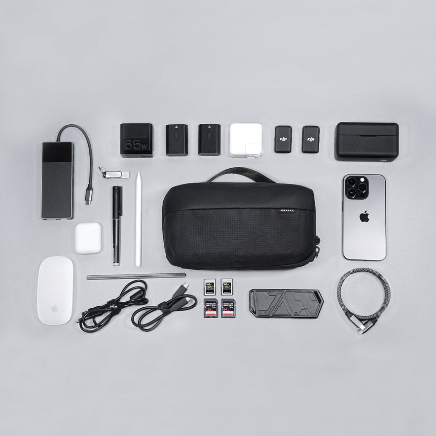 A neatly arranged flat lay features a Tech Pouch along with a smartphone, charging cables, adapters, memory cards, Apple Magic Mouse, digital pen, stylus, and other small gadgets on a light grey background.