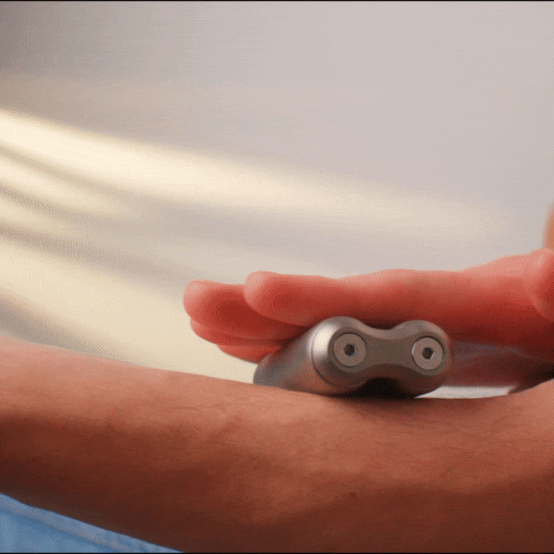Someone glides the handheld silver ONO Roller Titanium over their forearm, its sleek design standing out against a softly blurred background—an ideal fidget accessory and stylish addition to any desk.