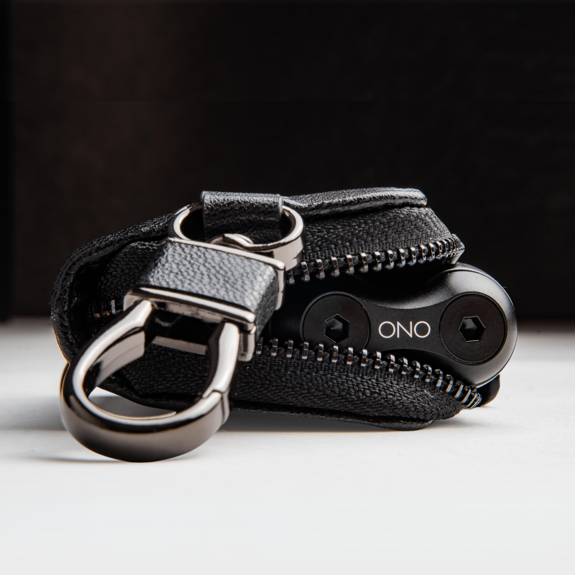 A close-up of the ONO Roller Premium Keychain Case shows it partially unzipped with a small black ONO tool inside, attached to a metal keyring. The case and tool rest on a light surface against a dark background.