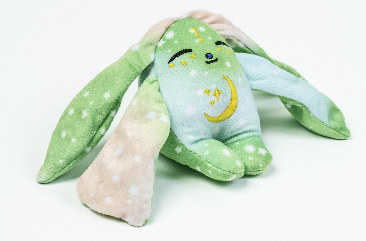 A Clover Mini Wrist Hugger – Magnetic Sensory Plush, shaped like a small green rabbit with long ears, embroidered closed eyes, and a yellow crescent moon and stars on its chest.