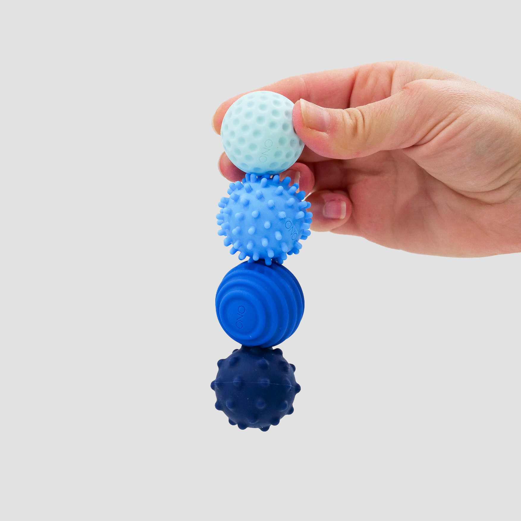 A hand holds four Signets, textured sensory balls in various blue shades, each with a distinct surface pattern for an engaging fidgeting experience, set against a plain light background.