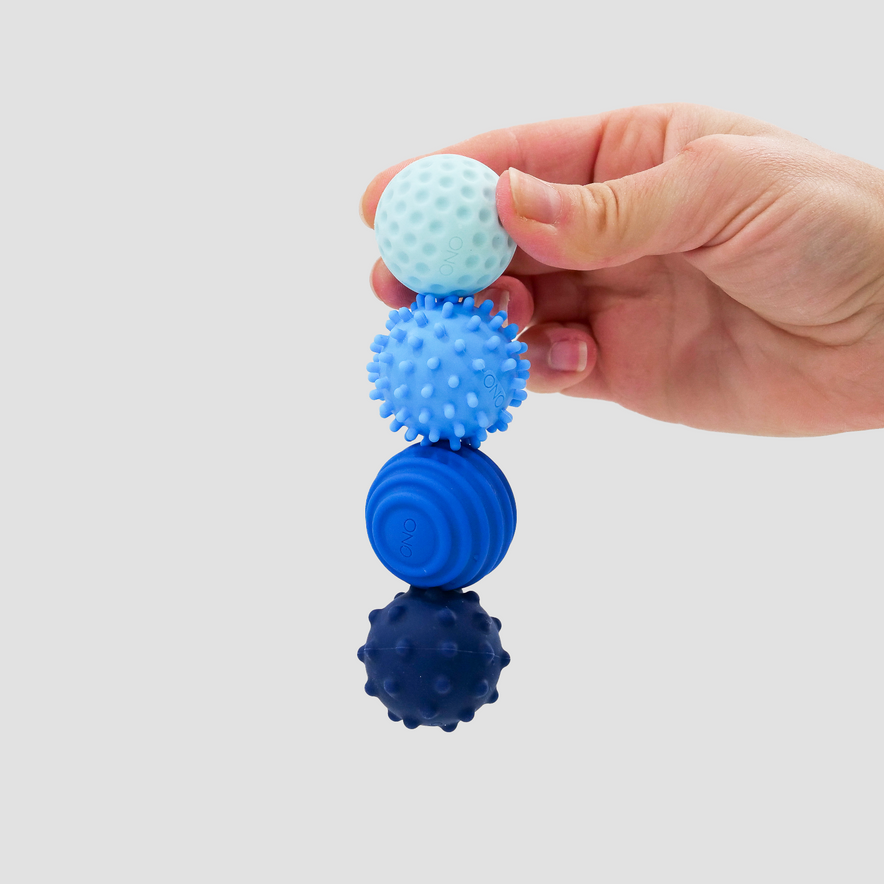 A hand holds four Signets, textured sensory balls in various blue shades, each with a distinct surface pattern for an engaging fidgeting experience, set against a plain light background.