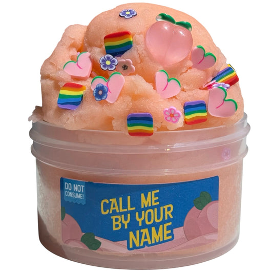 A 7 oz tub of Call Me By Your Name Peach Icee Slime with a peach scent, icee texture, and add-ins like rainbow hearts, flower charms, pink peach shapes. Label reads CALL ME BY YOUR NAME. Warning: DO NOT CONSUME!.