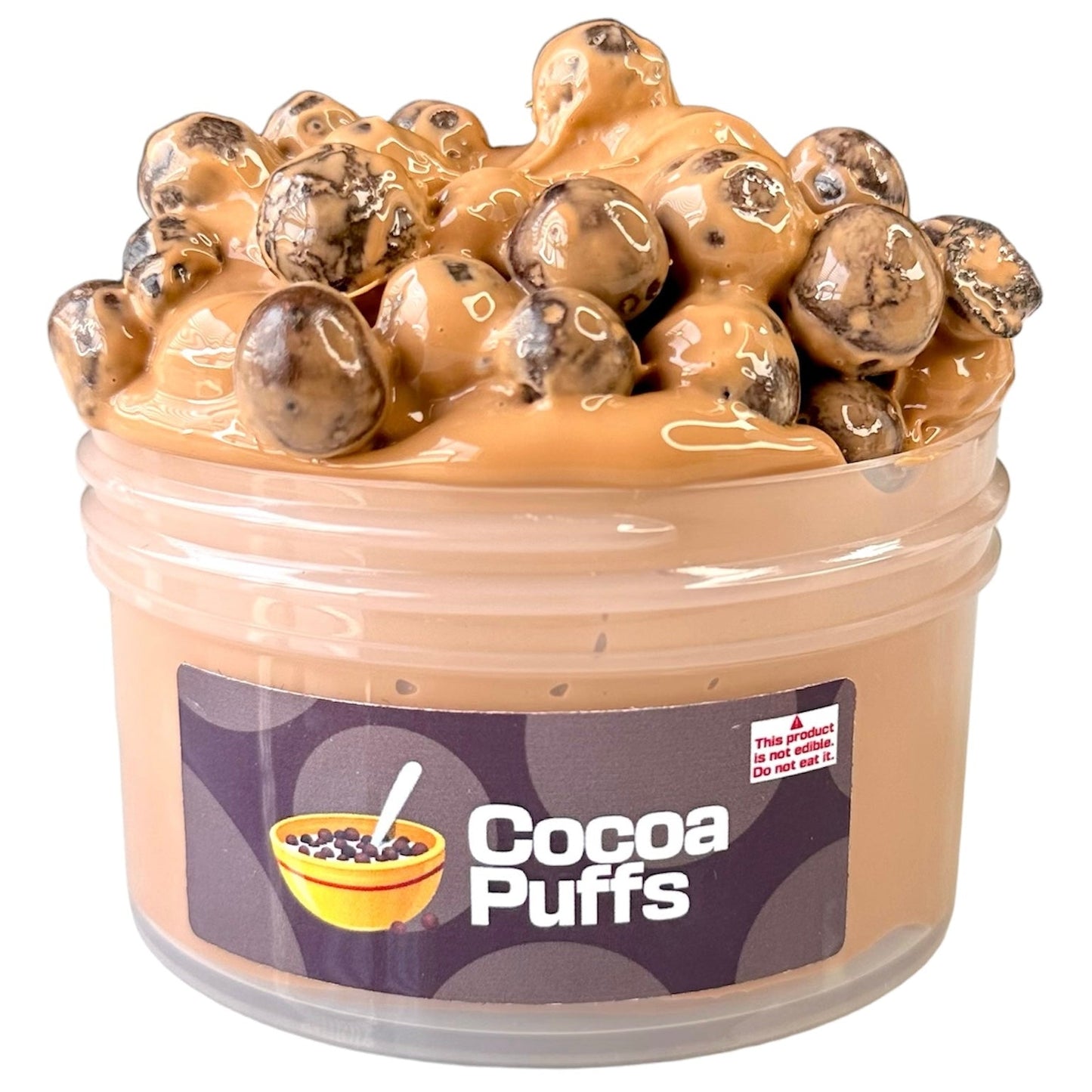 A small plastic jar labeled Cocoa Puffs contains thick tan pebble slime, topped with chocolatey beads resembling cereal. A warning sticker says: This product is not food. Do not eat it.