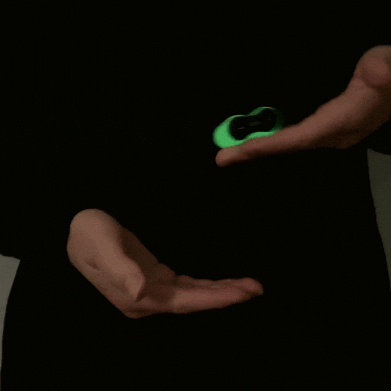 A person rolls the ONO Roller Soft Touch Plastic between their hands in the dark, its green glow standing out as it offers stress relief and sensory stimulation.