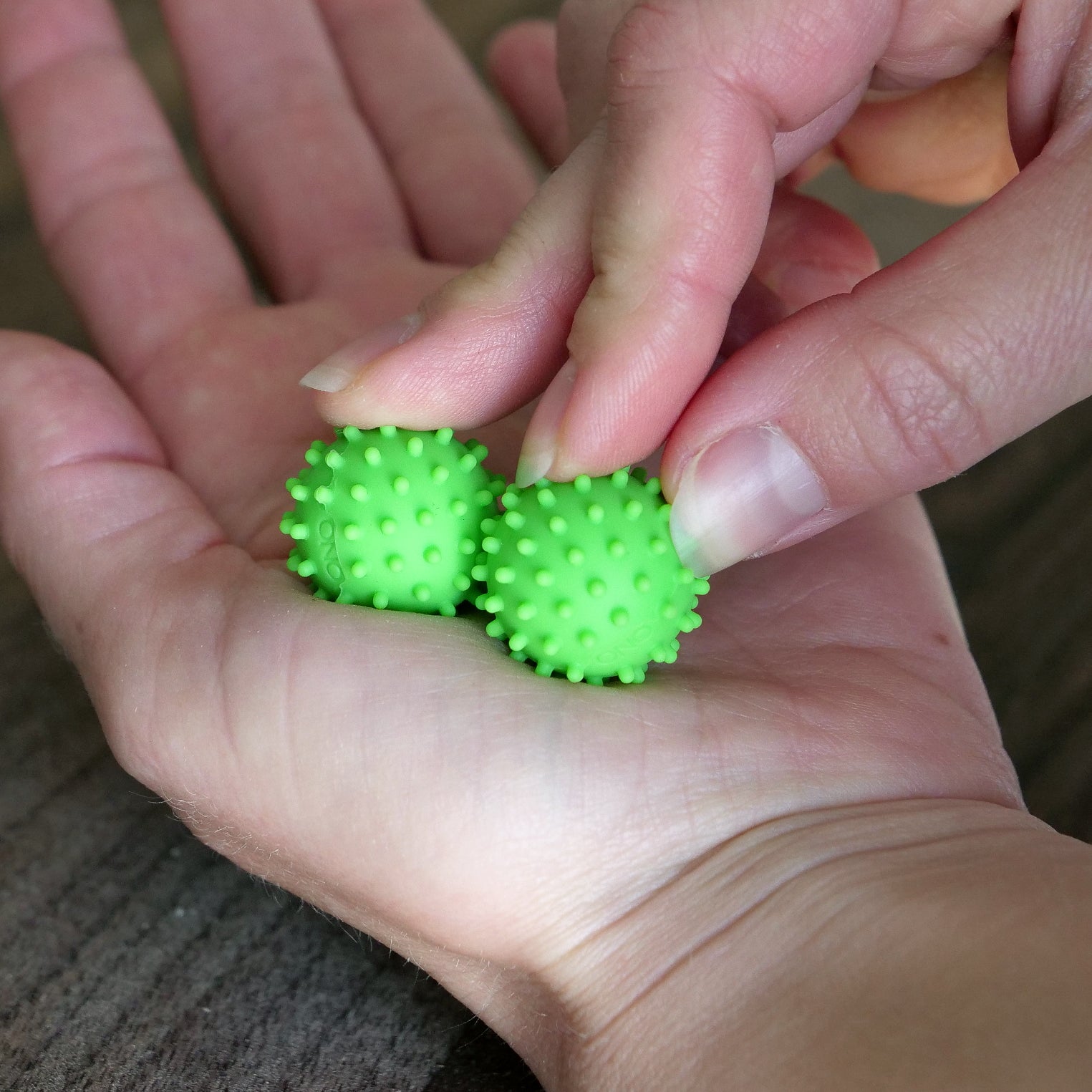 A person holds two small, green ONO Sigbits in their hand, pressing one against their palm with their fingers to enjoy sensory stimulation.