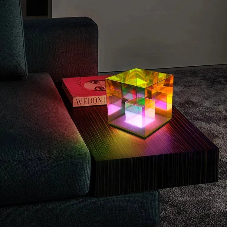 A Vibrant RGB LED Night Light for Parties and Home Décor sits on a dark wood side table next to a closed pink-covered book, beside a dark sofa in a cozy living room.