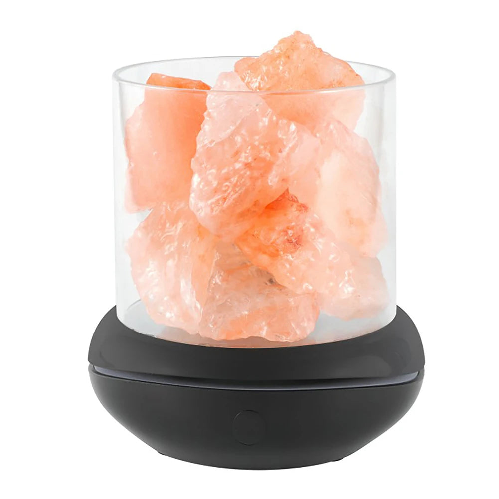 A clear glass container of large pink Himalayan salt crystals on a round black base serves as the Crystal Salt Lamp with USB Aroma Purifier & LED Multicolor Night Light, enhancing ambiance and purifying air in serene bedrooms.