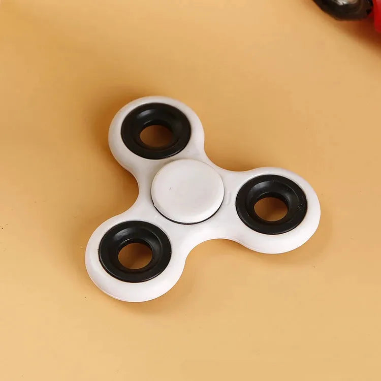 A white Premium ABS Tri-Spinner Fidget Toy for stress relief, ideal for all ages and perfect for autism and ADHD, with three rounded edges rests on a light brown surface.