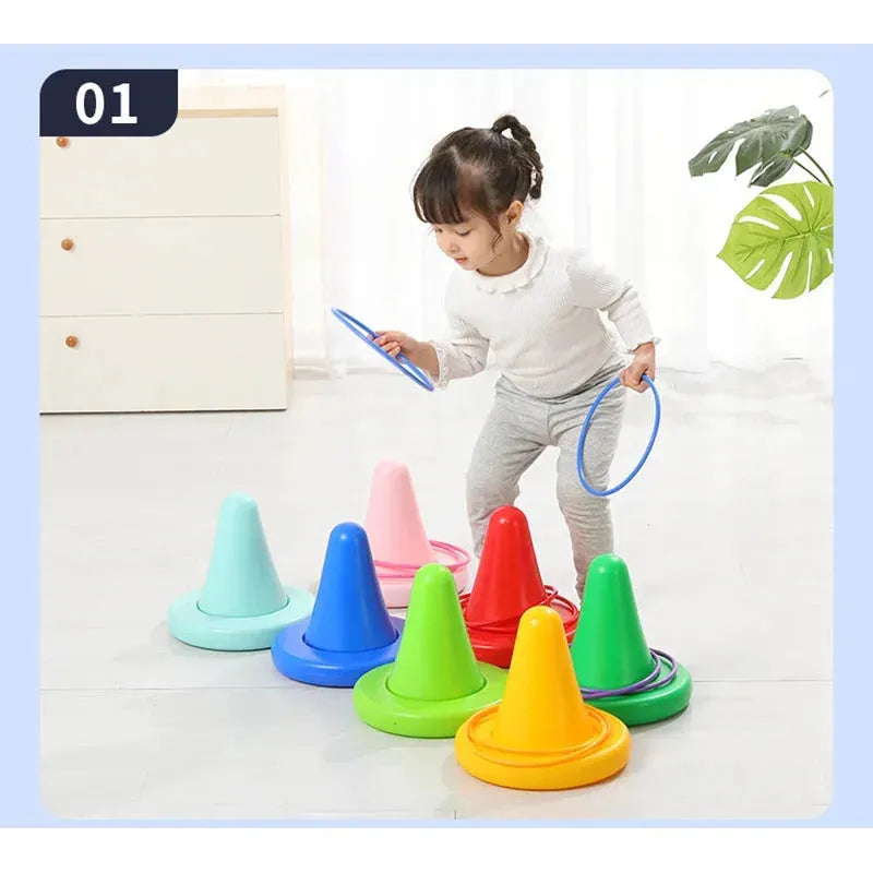A child is engrossed in a sensory game with the Kids Balance Training Unicorner Chair and colorful throwing rings, skillfully placing blue hoops on various cones indoors. Nearby are a potted plant and drawer.