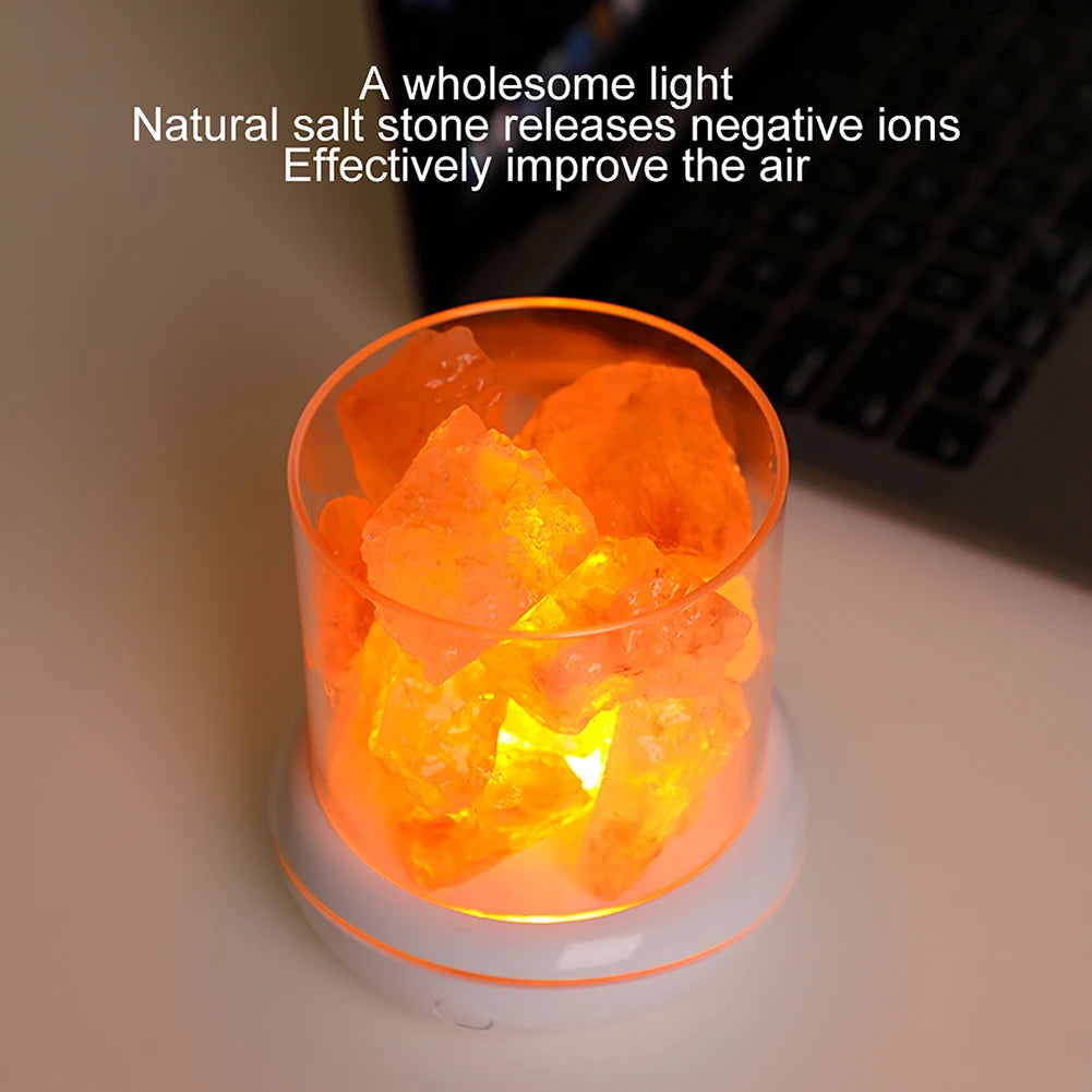 A Crystal Salt Lamp with USB Aroma Purifier & LED Night Light sits on a desk next to a laptop, emitting multicolor light while natural salt stones release negative ions to purify the air. Text reads: A wholesome light. Effectively improve the air with natural salt stone.