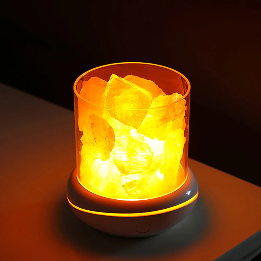 A Crystal Salt Lamp with a USB Aroma Purifier and LED Multicolor Night Light sits on a table, casting orange and yellow hues. The air purifier adds soothing scents as large salt crystals are illuminated, creating a unique ambiance in serene bedrooms.