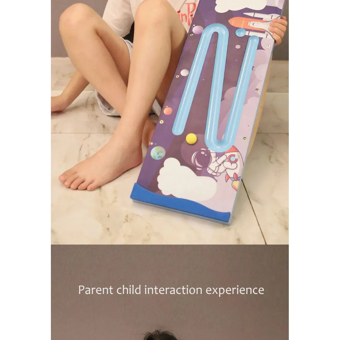 A child joyfully sits cross-legged, playing with the colorful Kids Wooden Balance Board. The blue zigzag marble path provides a sensory training adventure. Below, text reads Parent child interaction experience, highlighting their fun physical activity.