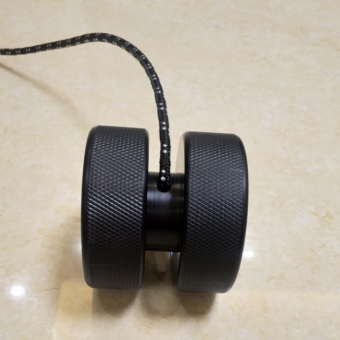 Close-up of two black wheels connected by an axle, each featuring an anti-slip grip. A black cable extends from the center, all on a light beige surface—ideal for a Finger Grip and Forearm Strength Trainer: Anti-Slip Wrist Impact Tool.