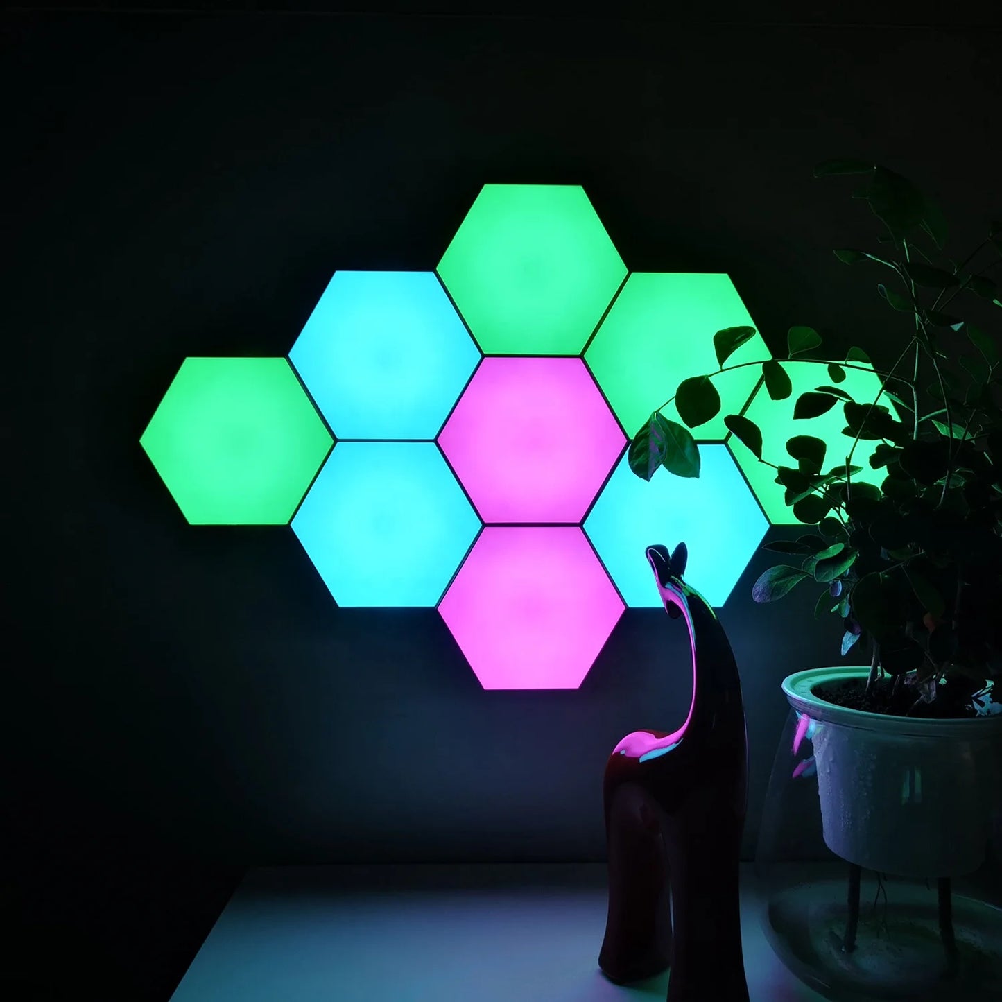 The Modular Hexagonal LED Wall Panels create an enchanting geometric pattern in green and purple hues. Paired with a potted plant and red abstract sculpture, these remote-controlled lights set the perfect mood or whimsical night light for any space with sensory support and calming ambiance.