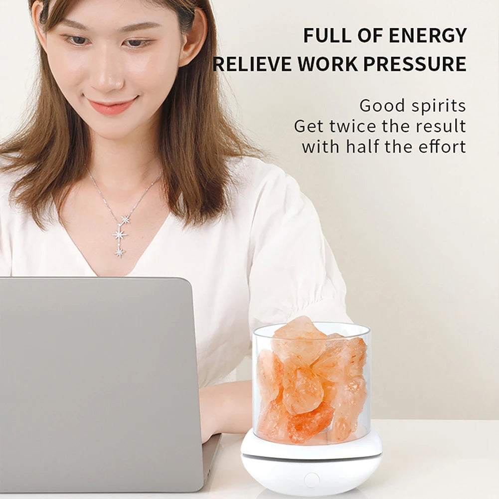 A woman sits at a desk smiling with a laptop. An aroma air purifier beside her diffuses calm, and a Crystal Salt Lamp with USB Aroma Purifier & LED Multicolor Night Light softly glows. Text reads: FULL OF ENERGY RELIEVE WORK PRESSURE. Good spirits. Get twice the result with half the effort.