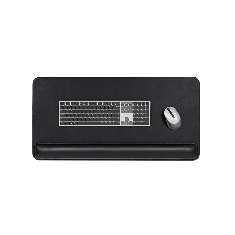 The Desk Mat Bundle features a black vegan leather desk mat, silver keyboard, matching ergonomic wrist cushion, and gray wireless mouse, all displayed from a top-down view centered on a white background.