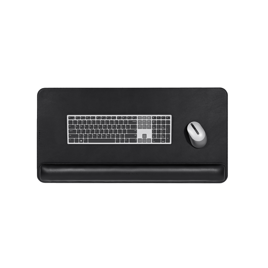The Desk Mat Bundle features a black vegan leather desk mat, silver keyboard, matching ergonomic wrist cushion, and gray wireless mouse, all displayed from a top-down view centered on a white background.