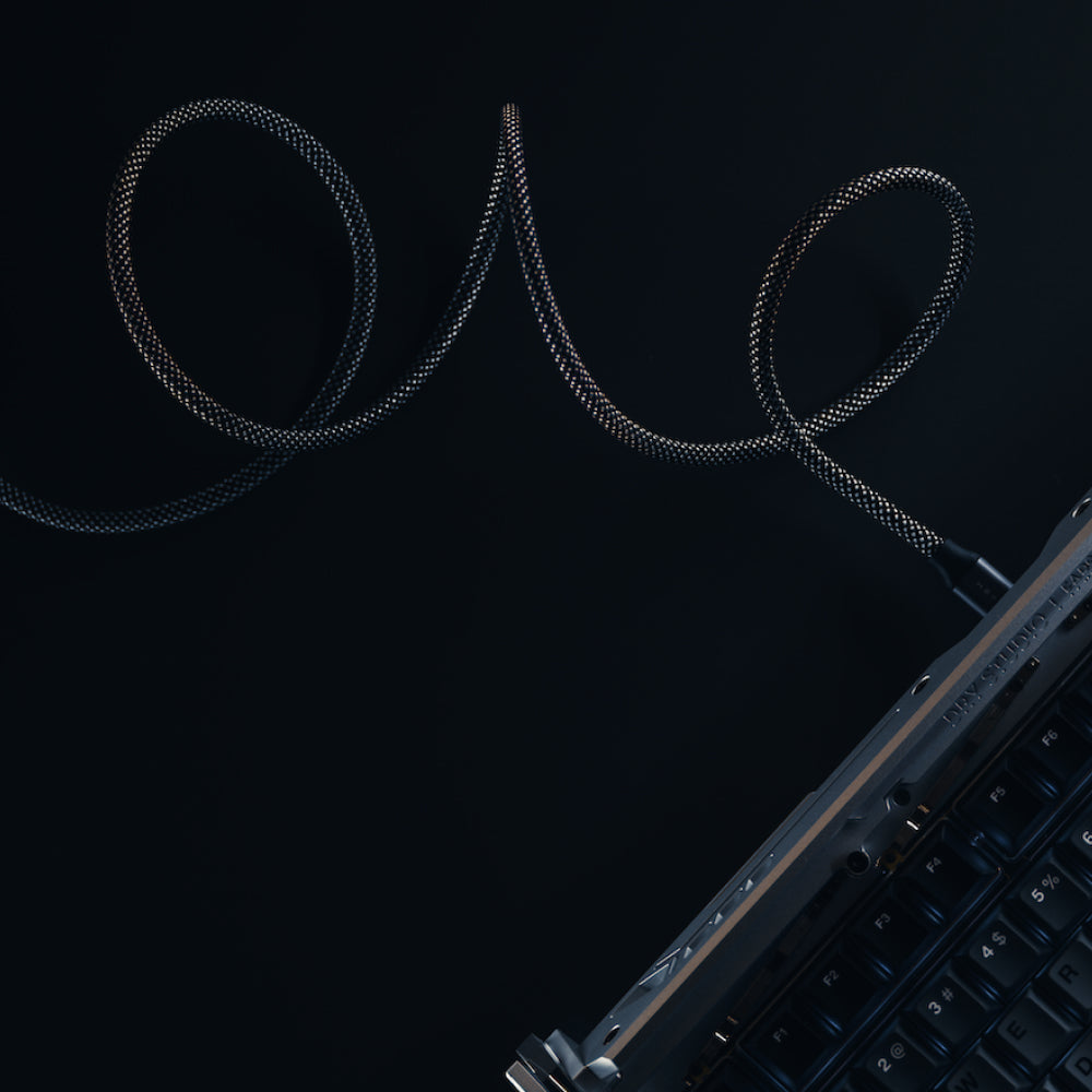 A close-up of a mechanical keyboard with a Magnetic Charging Cable, featuring a coiled, braided USB-C connector extending from the top right, set against a dark background.