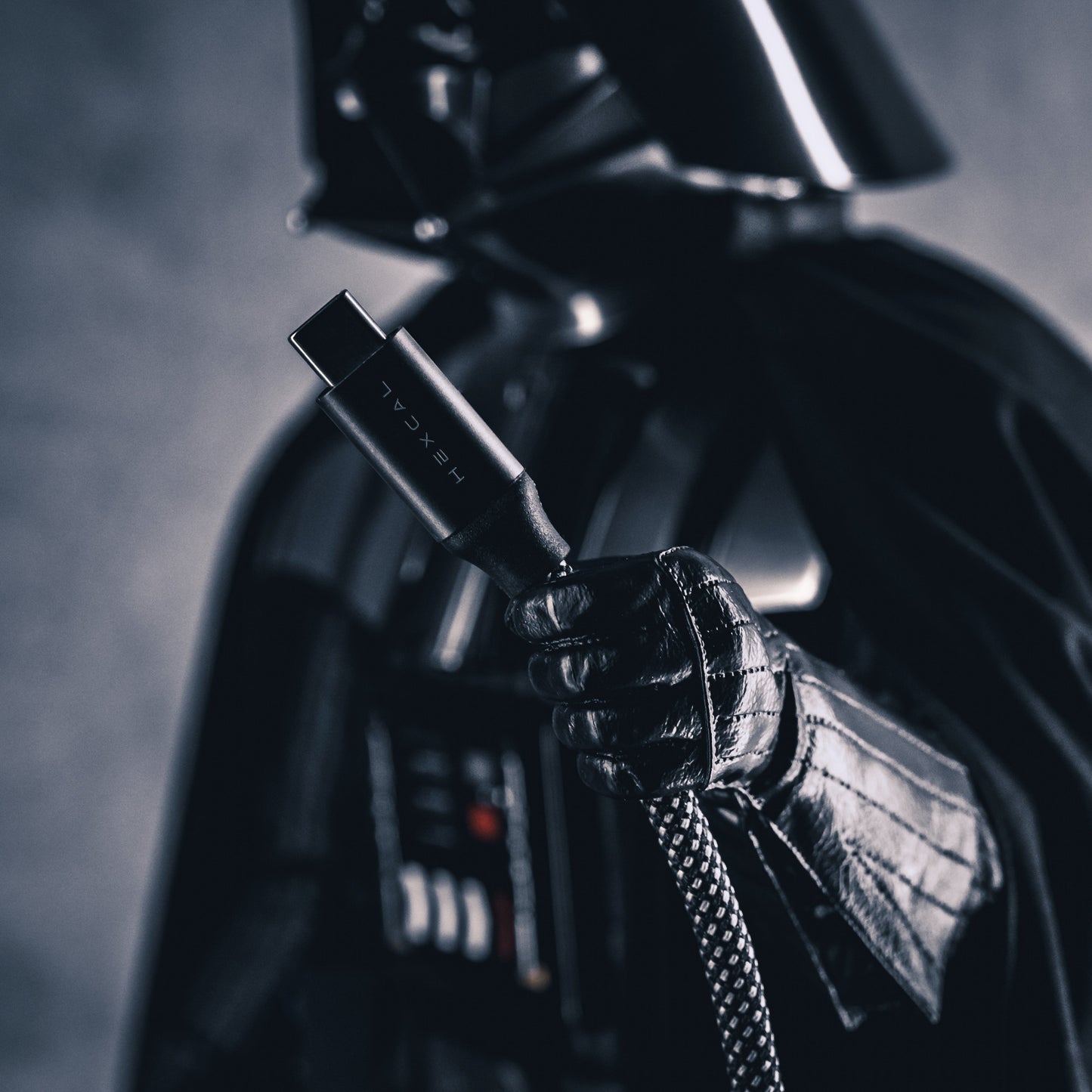 A person in a black, futuristic costume holds a Magnetic Charging Cable, its connector in focus and labeled “HEXCAL,” showcasing advanced USB-C Power Delivery, with a blurred background.