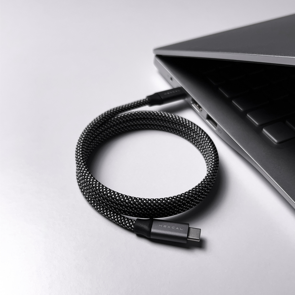 A Magnetic Charging Cable is coiled next to a sleek, partially open laptop on a white surface. The cable is connected to one of the laptop’s ports.