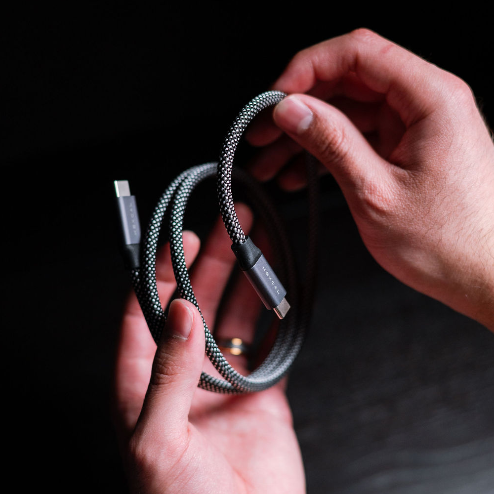 Two hands hold a Magnetic Charging Cable against a dark background. The coiled cable shows both connectors, illustrating its magnetic feature and compatibility with USB-C Power Delivery devices.