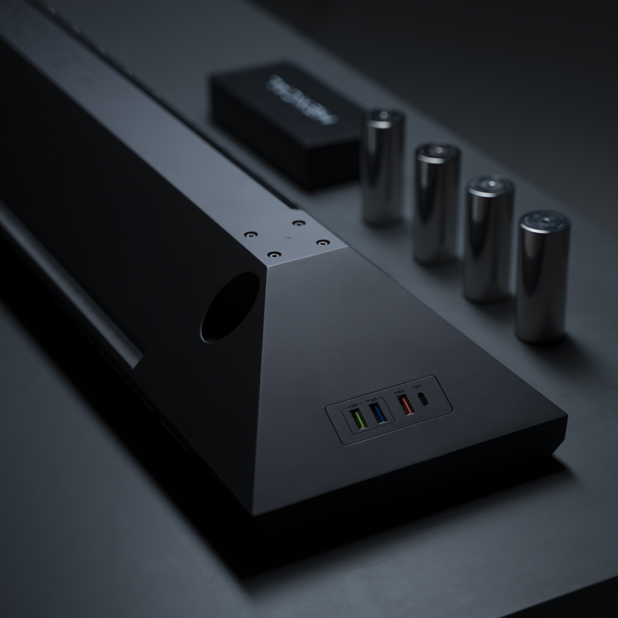 The Hexcal Studio™—a sleek black device with multiple colored USB ports, a compact black box, and four metallic batteries—adds style and function to any workstation, ideal for those who value organized, modern tech setups.