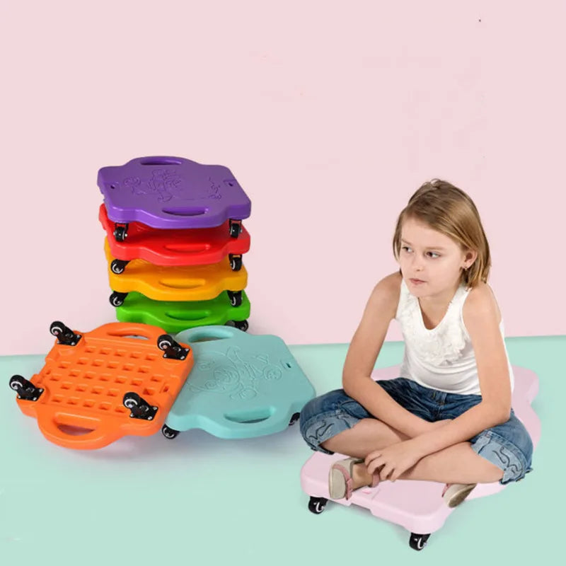 A girl in a white shirt and jean shorts sits on a purple Kids Sensory Balance Board - Four-Wheeled Skateboard, ideal for motor skill development. She is surrounded by colorful boards in pink, green, orange, and red against a pink and light blue backdrop.