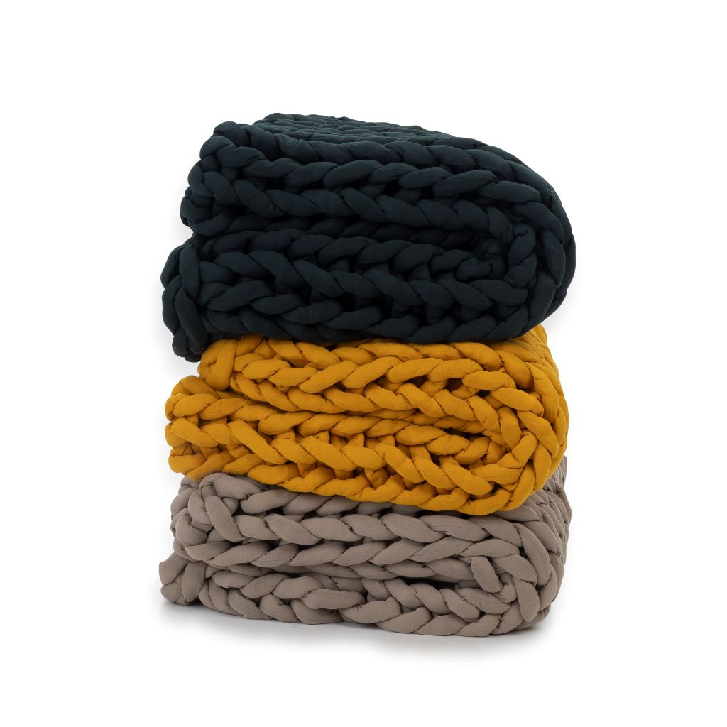 Three Knit Weighted Blankets are stacked: a dark green super soft weighted blanket on top, mustard yellow in the middle, and light taupe on the bottom—each features thick, braided yarn textures for cozy warmth.