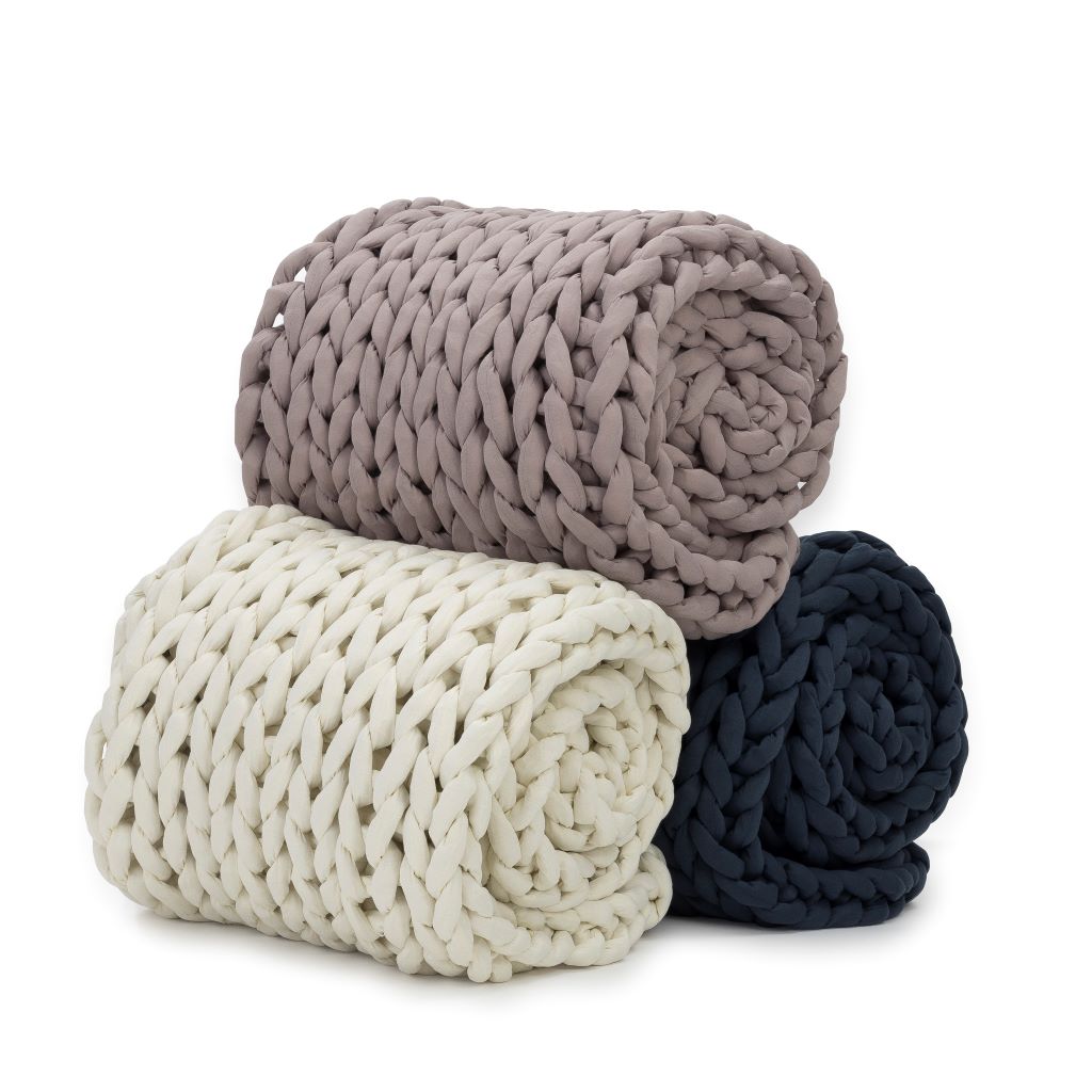 Three Knit Weighted Blankets—light taupe, cream, and dark navy blue—are rolled up and stacked together. Each super soft blanket rests on a plain white background.