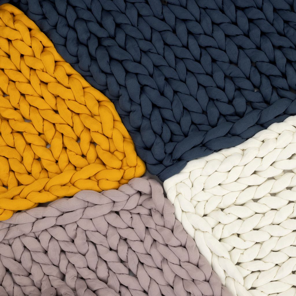 Close-up of the Knit Weighted Blanket crafted in breathable chunky knit, featuring yellow, navy blue, white, and light gray triangular sections meeting at the center to create a bold geometric pattern.