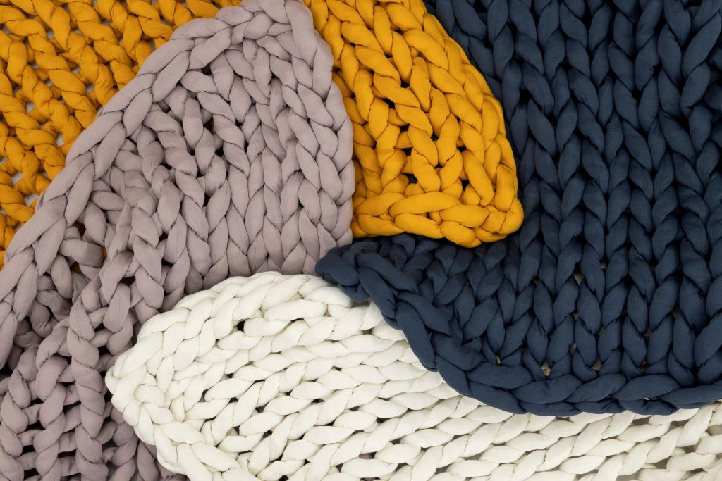 Close-up of chunky Knit Weighted Blankets in mustard yellow, navy blue, lavender, and cream—layered for a textured, cozy look. Enjoy the comfort and calming effect of a super soft weighted blanket with this inviting display.