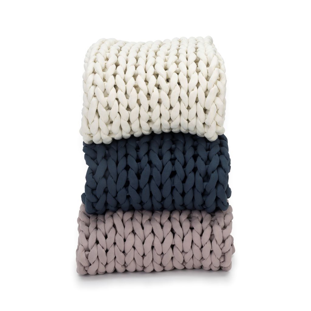 Three Knit Weighted Blankets are stacked neatly: white on top, dark blue in the middle, and light gray at the bottom. Each features a thick woven texture and is displayed against a white background.