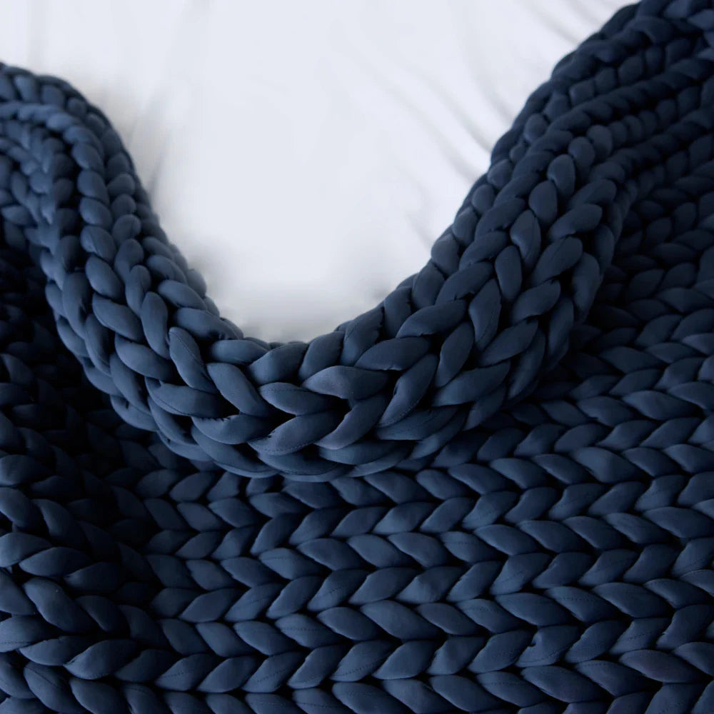 A close-up of the Ice Knit Weighted Blanket in Pacific Blue, featuring large, thick stitches and draped on a white surface.