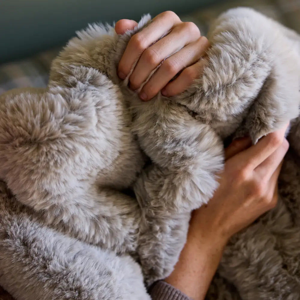 Two hands gently grasp the Snuggle Luxe Blanket in Earl Grey, showcasing its plush texture and cozy faux fur for ultimate comfort.