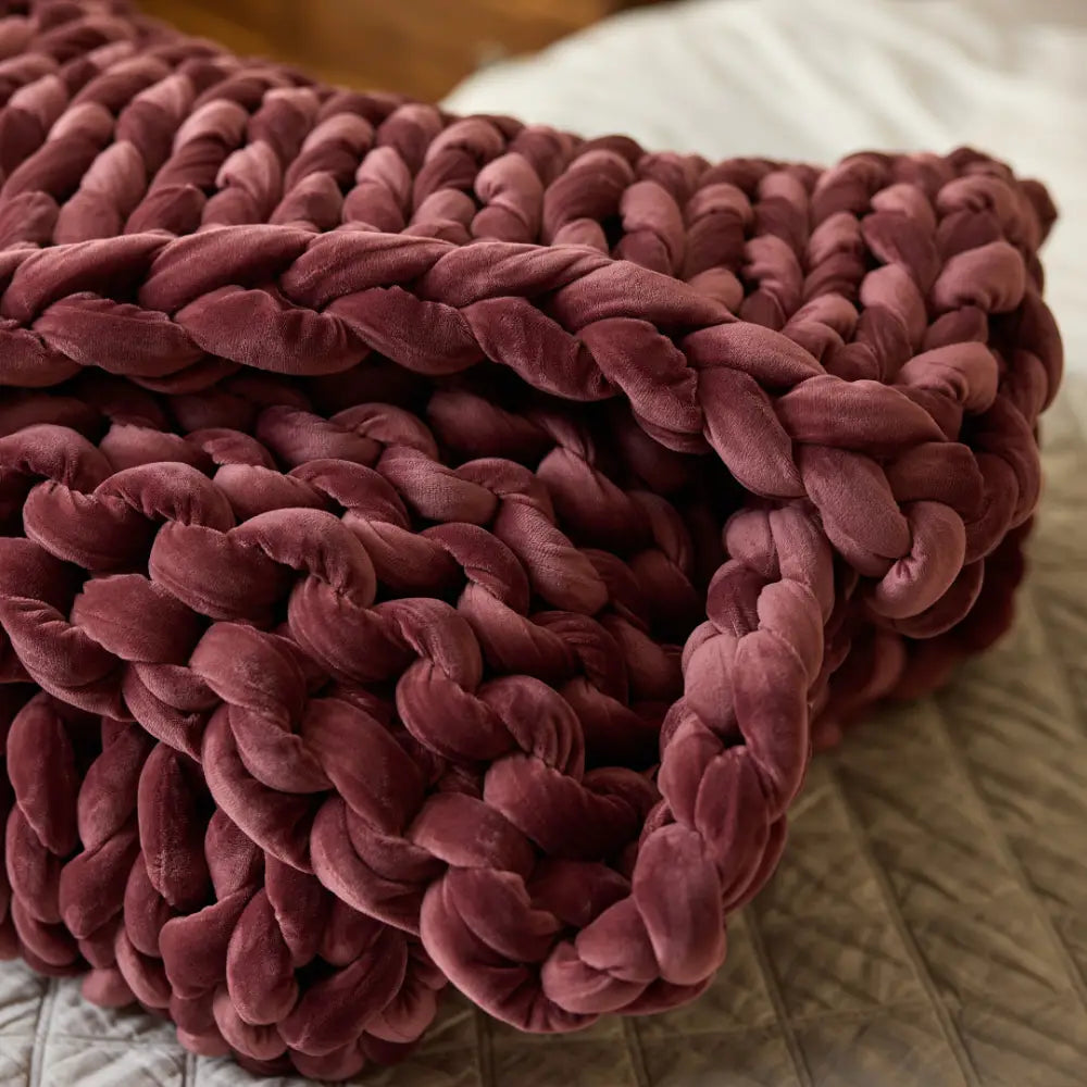 A close-up of the Velvet Weighted Blanket in deep burgundy, folded neatly on a textured light bedspread, radiates cozy comfort.