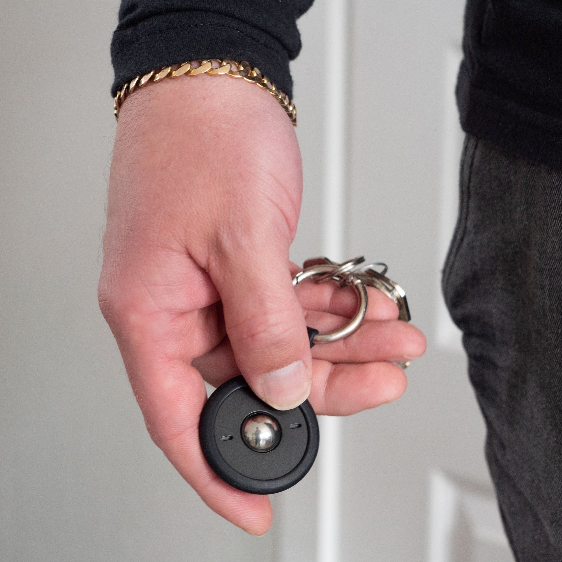 A person with a black sleeve and gold bracelet holds keys featuring a round black electronic key fob and the ONO Scroller Aluminum sleek fidget keychain.