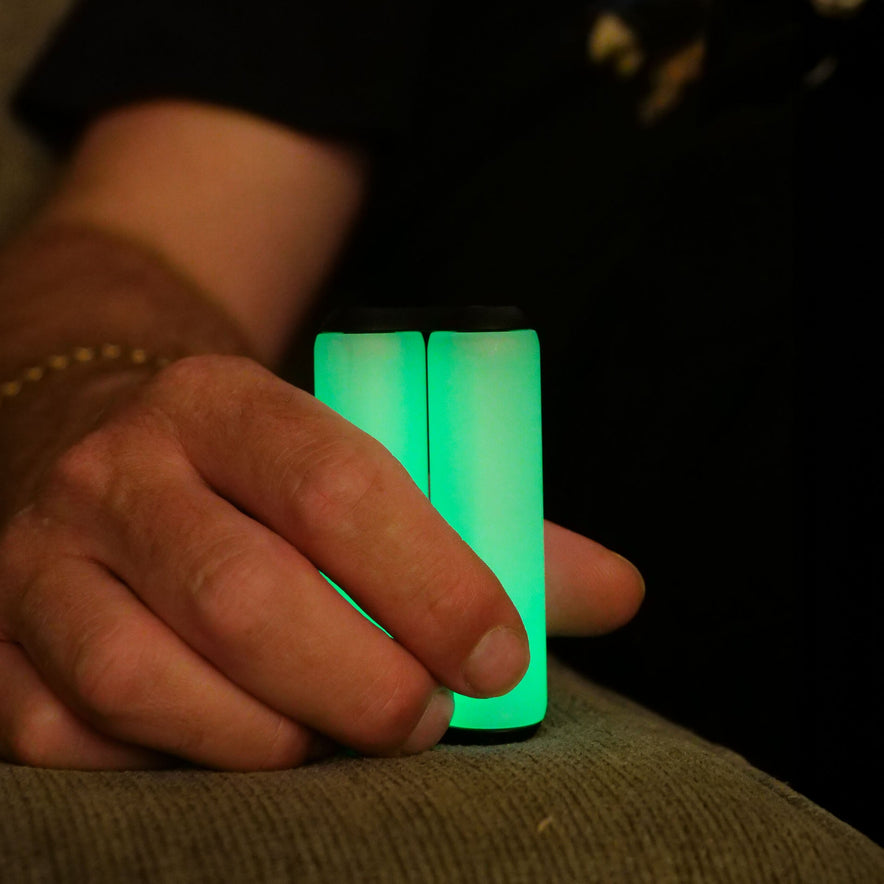 Someone holds two ONO Roller Soft Touch Plastic stress relief sticks in their hand while sitting on a couch, with a dark background.