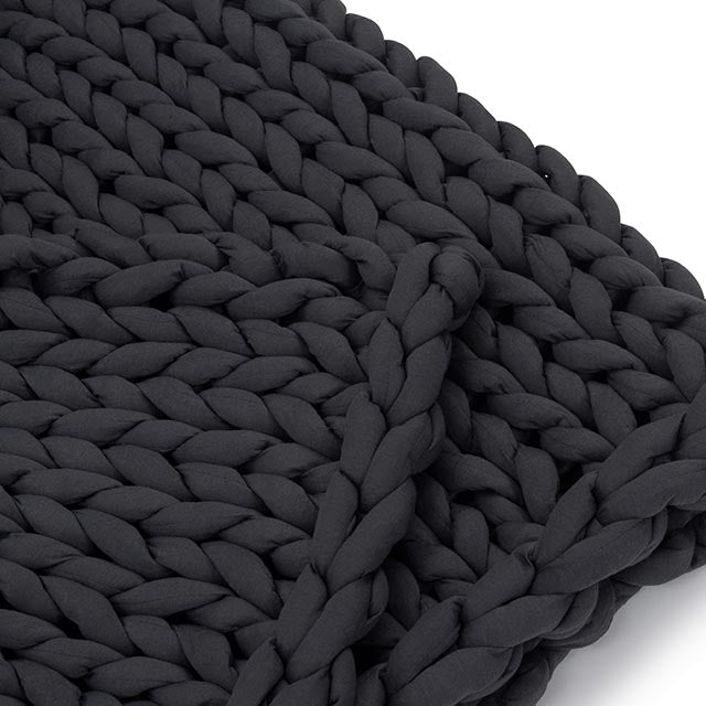 A close-up of the Knit Weighted Blanket, a chunky, black hand-knitted blanket made from thick, soft yarn for breathability, shown against a white background.