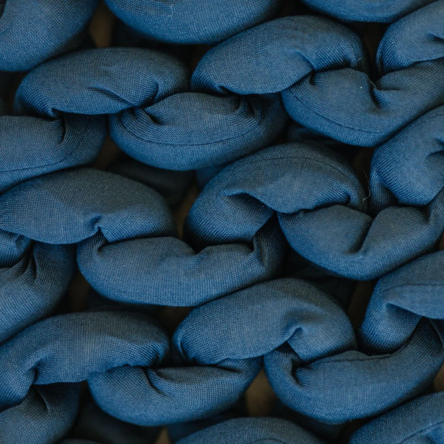 Close-up of thick, soft blue strands woven together in a chunky braid, showcasing the textured surface of the Knit Weighted Blanket.