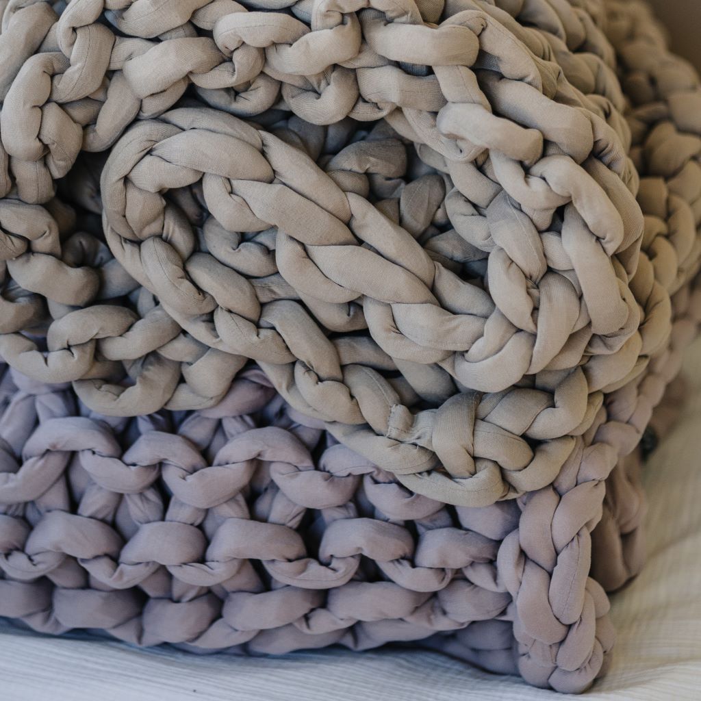 A close-up of the Knit Weighted Blanket, rolled up on a flat surface. Its thick, light gray yarn gives a cozy, textured look thats perfect for comfort and relaxation.