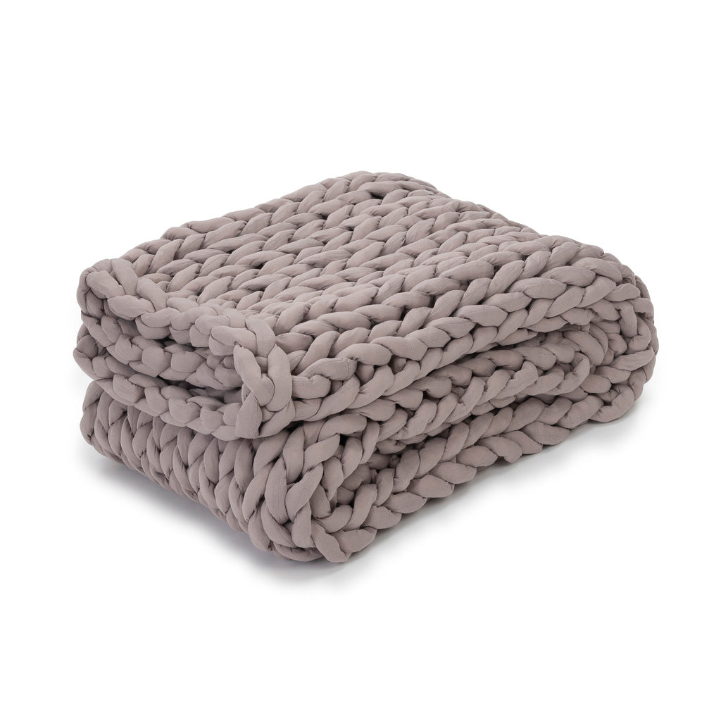 A chunky, hand-knitted Knit Weighted Blanket in Dusty Rose is neatly folded, highlighting its thick braided texture and soft, cozy look.