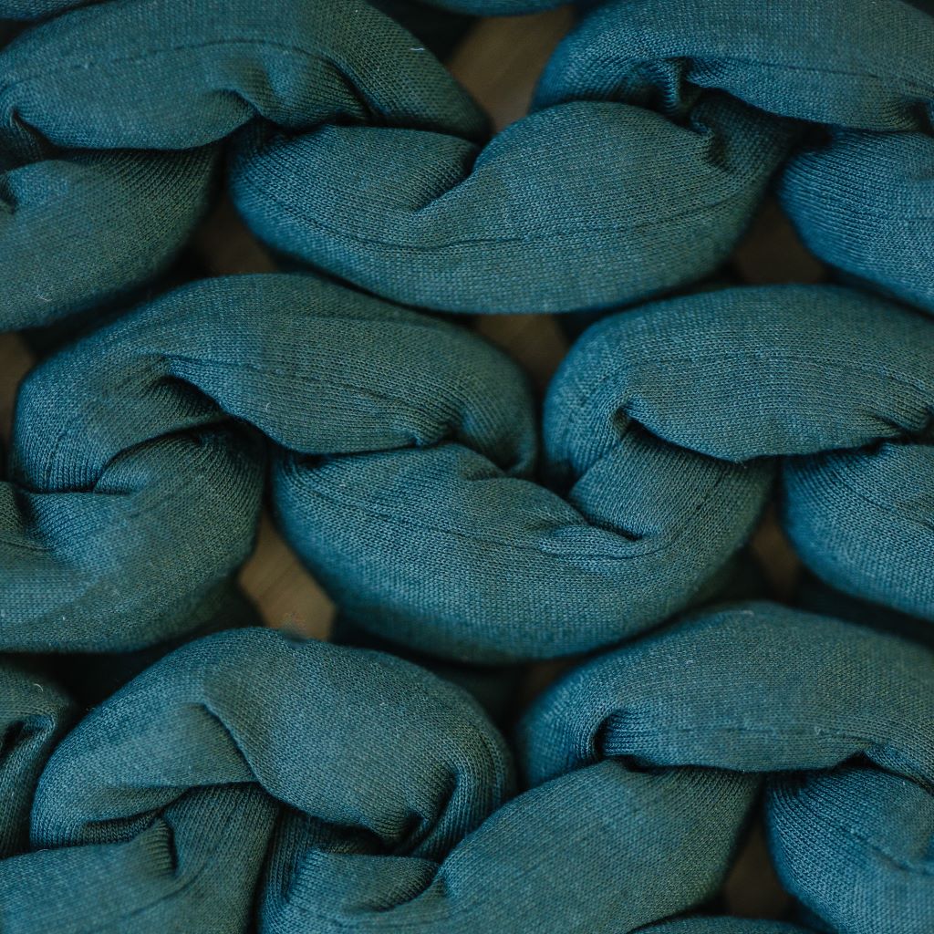 Close-up of thick, teal strands woven in a chunky braided pattern showcases the textured and cozy look of the Knit Weighted Blanket.