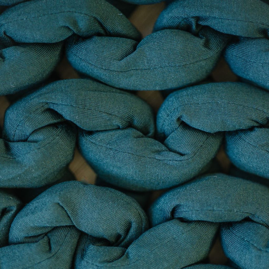 Close-up of thick, teal strands woven in a chunky braided pattern showcases the textured and cozy look of the Knit Weighted Blanket.