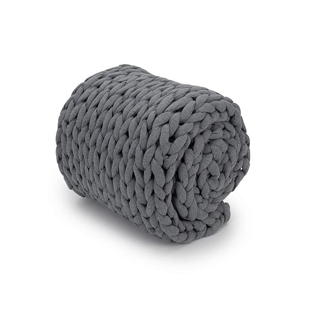 The Knit Weighted Blanket, featuring a chunky dark gray braided design, is rolled up on a white background.